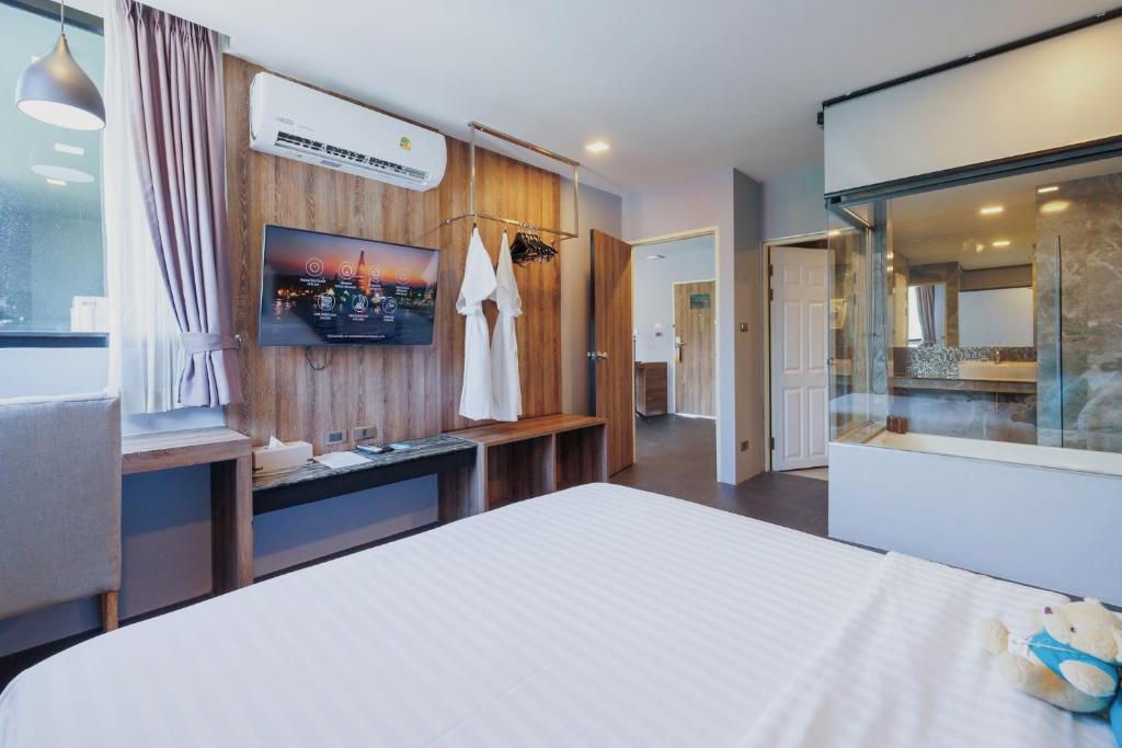 A bed faces a wood-panelled media wall, with a glazed bathtub area beside the sleeping space.