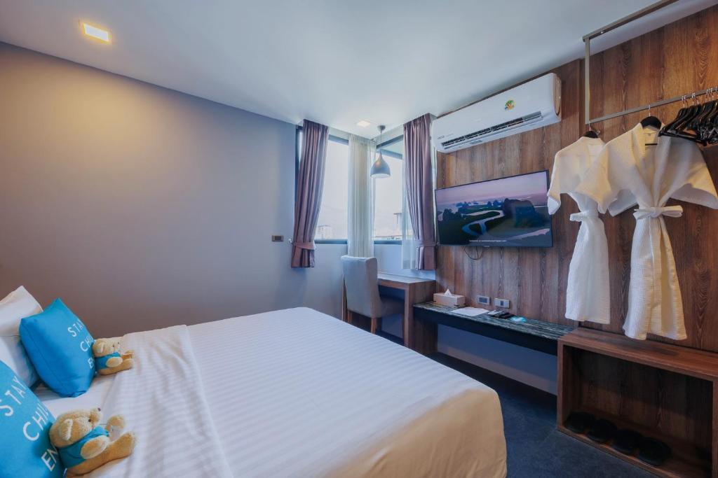 A compact bedroom combines a double bed, small desk, wall-mounted TV and open clothes rail.