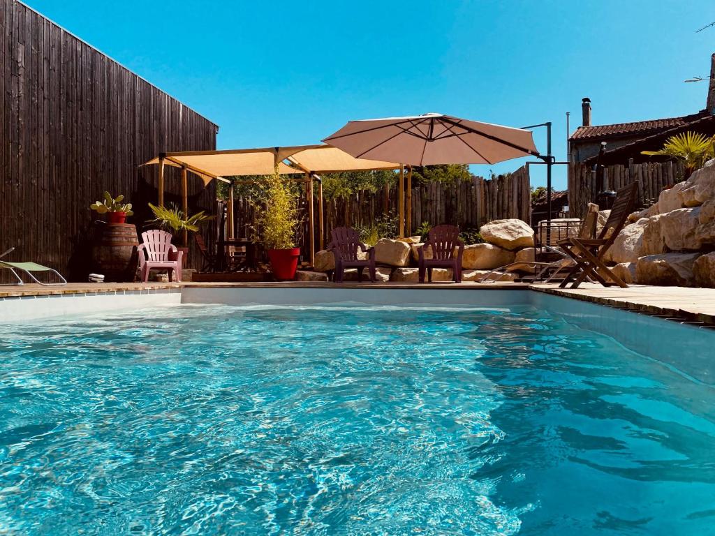 a swimming pool with an umbrella and some chairs at La Salamandre Enchantée in Louzac - Saint-André