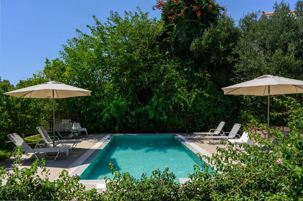 a swimming pool with two umbrellas and two chairs at Koxyli Studios & Apartments in Kaligata