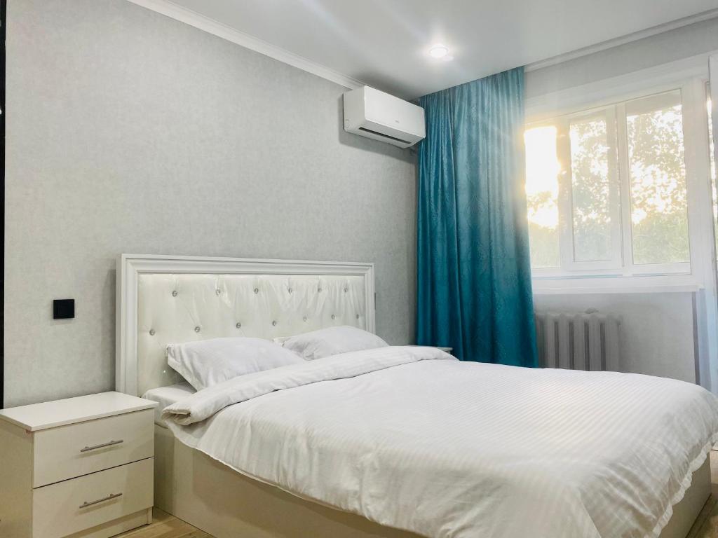 a bedroom with a white bed with a blue curtain at Elegant Home Apart in Karagandy