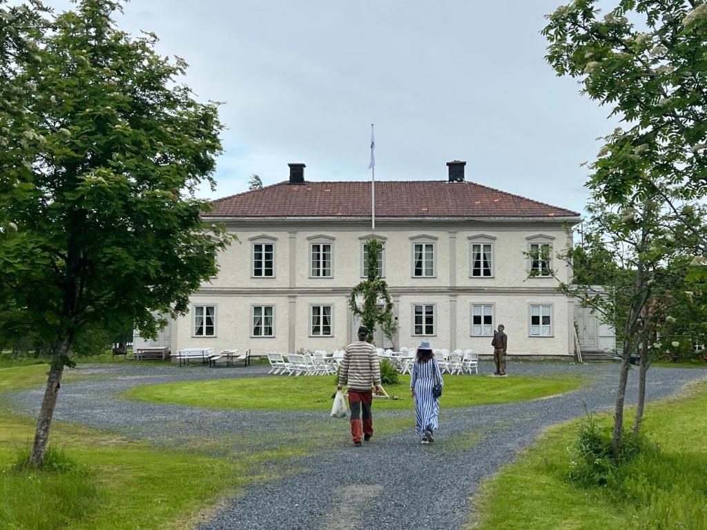 two people walking down a gravel road in front of a white house at Huså Herrgård in Järpen