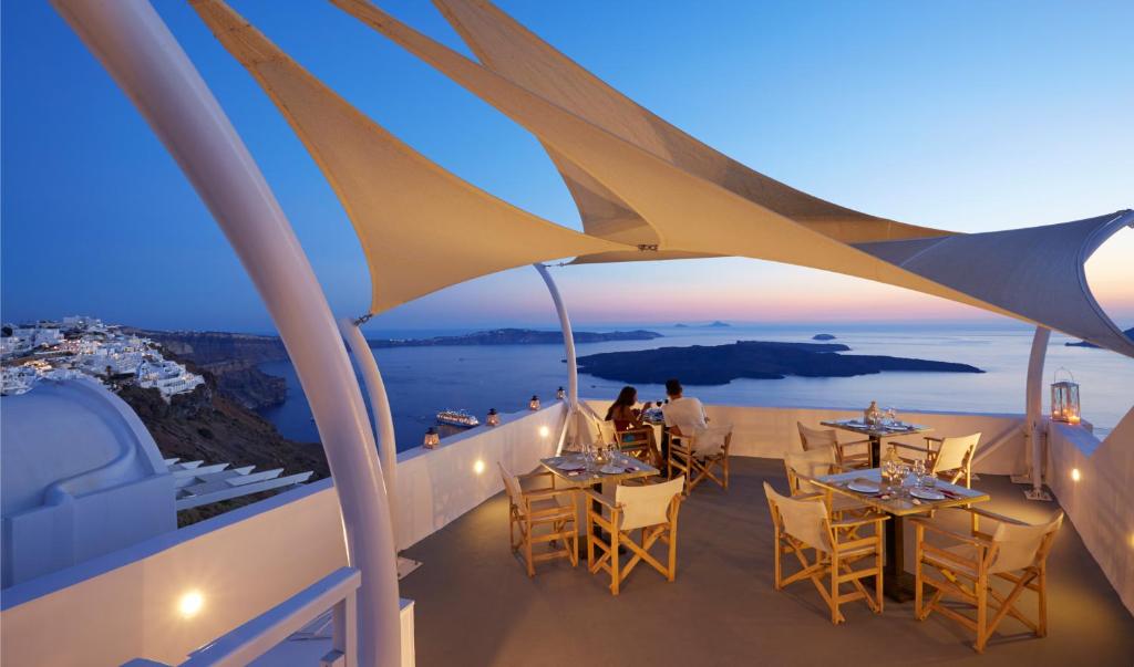 a balcony with tables and chairs and a view of the ocean at Ira Hotel & Spa in Firostefani