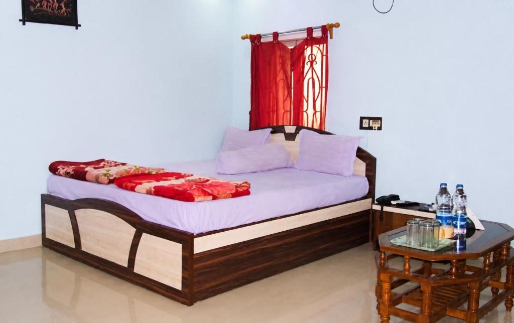 a bedroom with a bed with a red curtain and a table at Hotel Alankar Lodge Kharagpur in Kharagpur