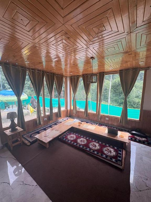a living room with a wooden ceiling and a large window at Gaunnie Valley - Jibhi in Jibhi