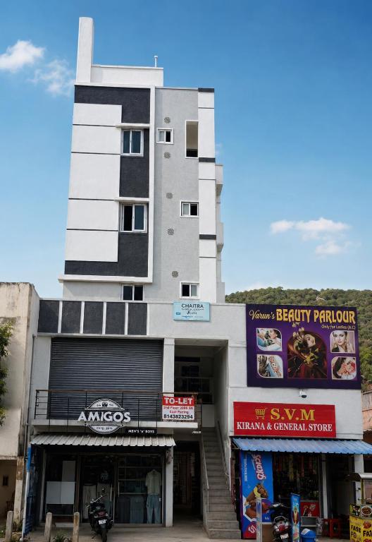 a tall white building with some shops in front of it at Venya Vihar Vizag MVP AC Deluxe 1 BHK Studio Apartment in Visakhapatnam