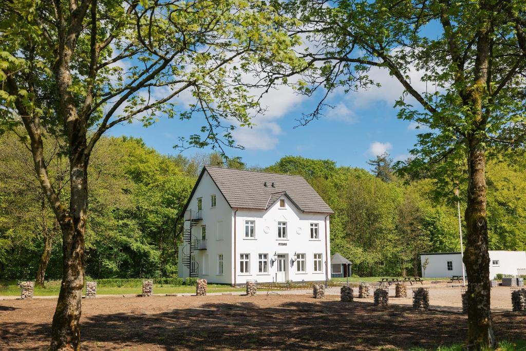 a white house with trees in the foreground at Velling Koller Hotel og Camping in Bryrup