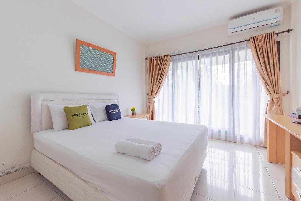 a white bedroom with a large white bed and a window at Urbanview Hotel Tridaya Cisarua Puncak in Kopo 2