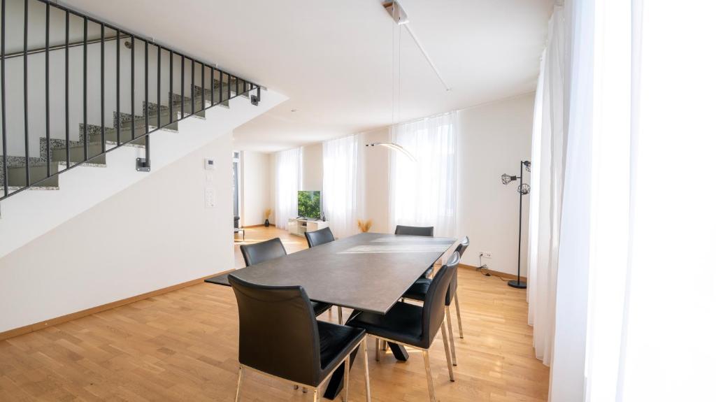 a dining room with a table and chairs and a staircase at Swiss Suites Oberglatt in Oberglatt