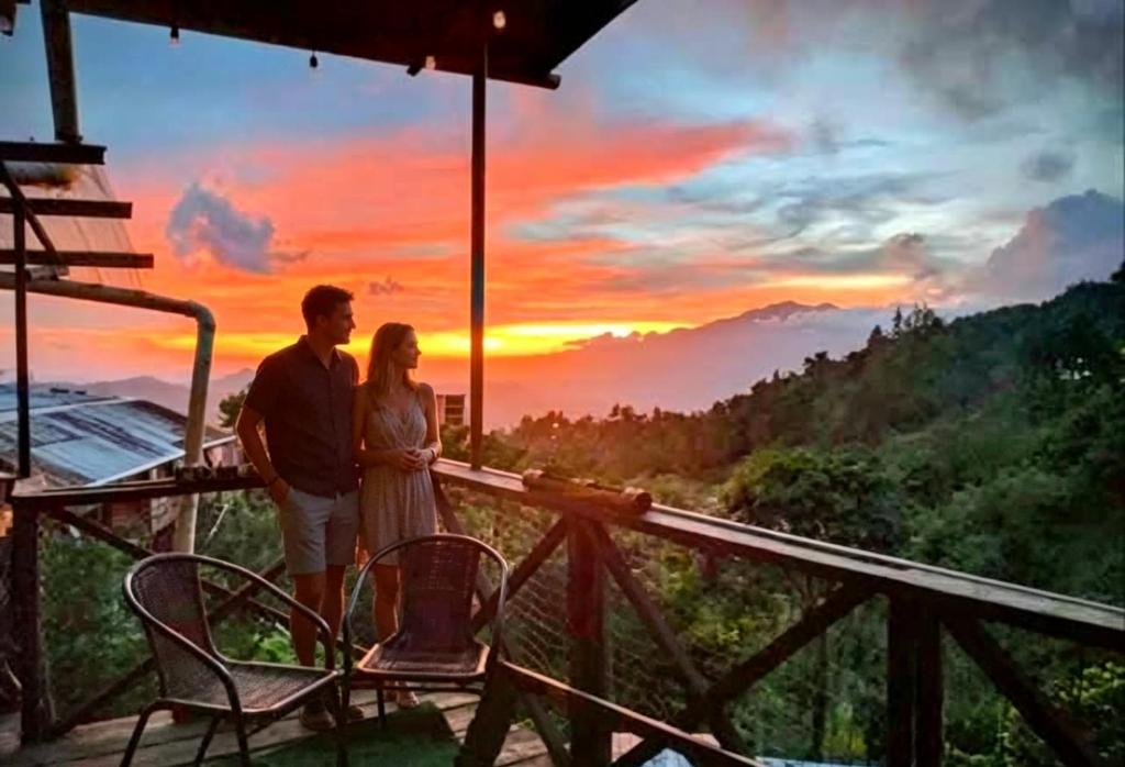 a man and woman standing on a balcony with the sunset at Roots Casa Rústica in Valle Hornito