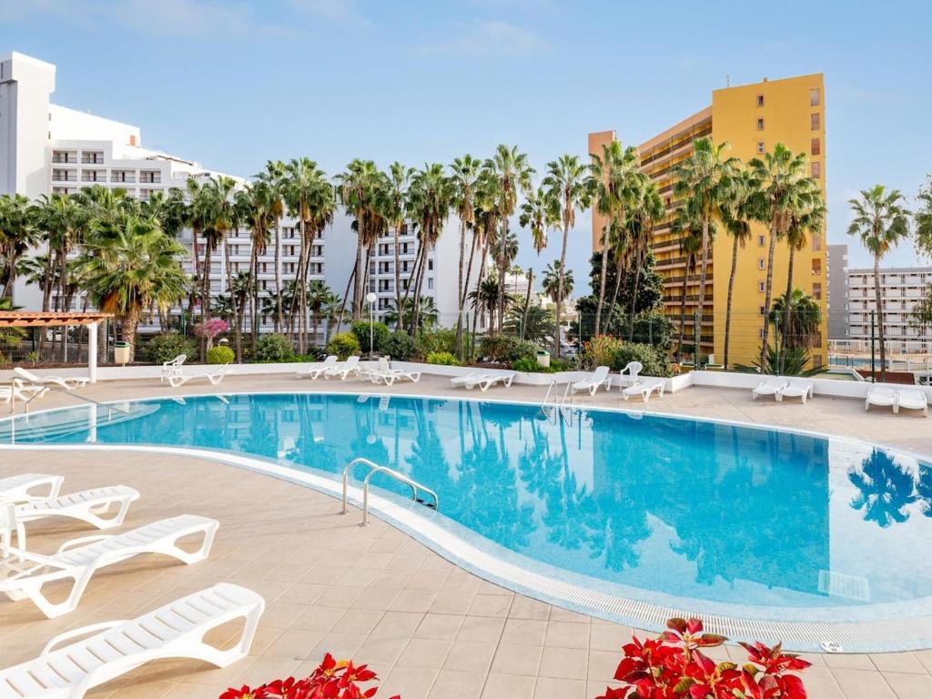 a swimming pool with chairs and palm trees and buildings at Cute Las Flores 1i with pool in Costa de Adeje