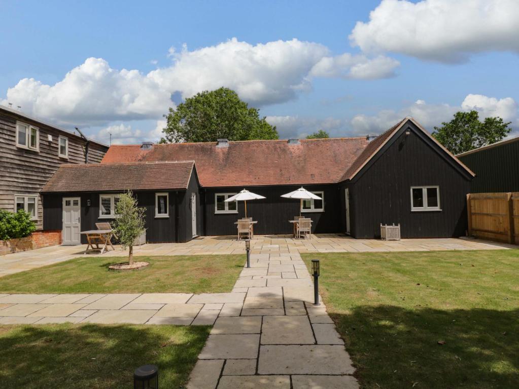 a black barn with tables and umbrellas in a yard at Poppy Patch in Bicester