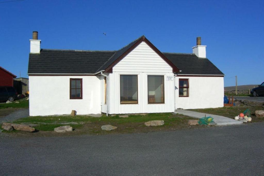 a small white house sitting on the side of a street at Fishers Croft in Hamnavoe