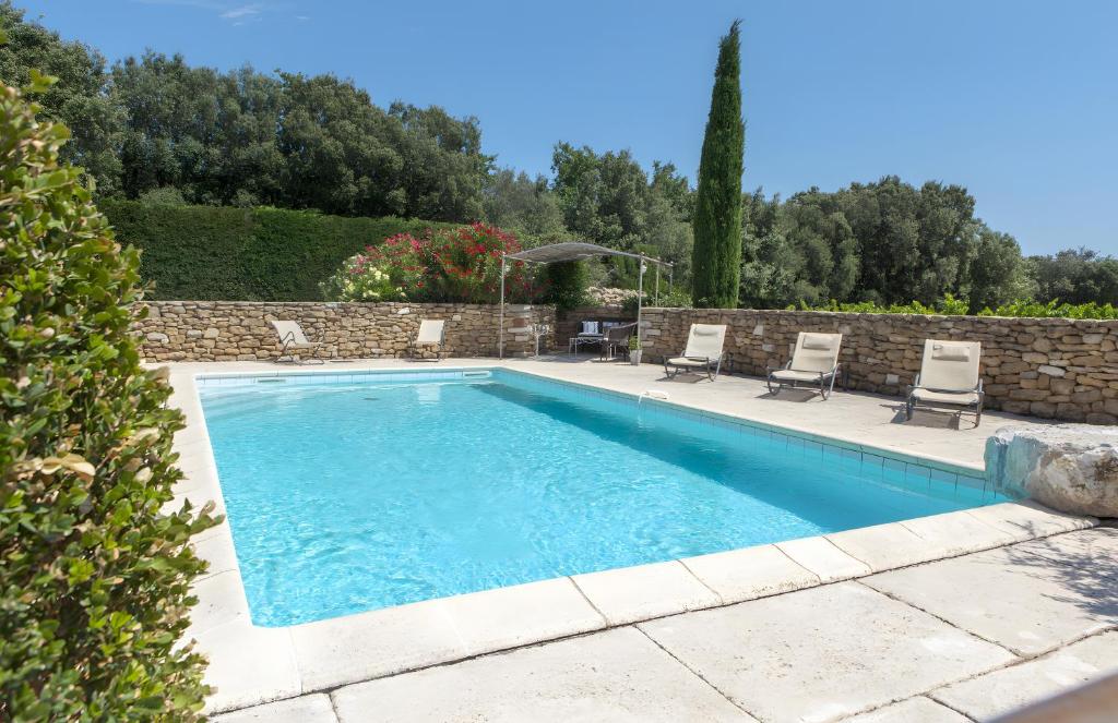 a swimming pool with chairs and a stone wall at Le Petit Mas - Piscine Clim in Grillon