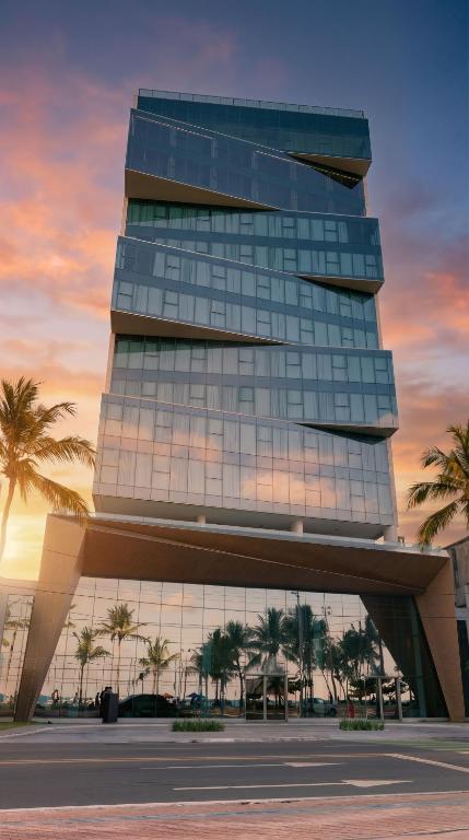 a tall glass building with palm trees in front of it at Sais Beach Living Hotel in Maceió