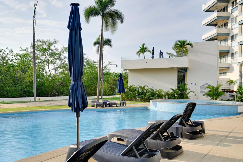 a hotel swimming pool with chairs and an umbrella at Explore Nature & Beaches! Nuevo Nayarit Condo in Nuevo Nayarit