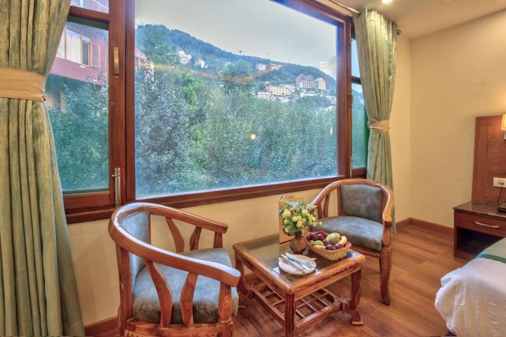 a room with two chairs and a table and a window at Gaunney Valley - Tirthan Valley in Manāli