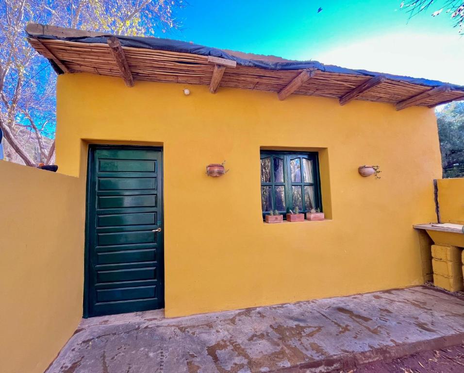 a yellow house with a green door and two windows at Tale Cabaña de campo in Huacalera