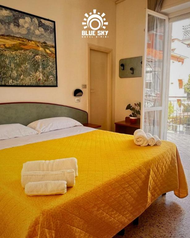 a bedroom with a yellow bed with towels on it at HOTEL BLUE SKY in Rimini
