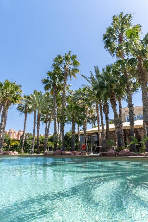 a pool with palm trees in front of a building at Hotel Alicante Golf in Alicante