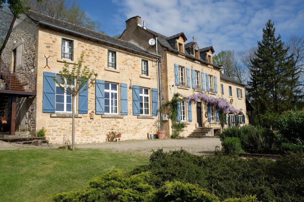 ein großes Backsteinhaus mit blauen Fenstern und lila Krätzen in der Unterkunft Le Couvent de Neuviale in Parisot