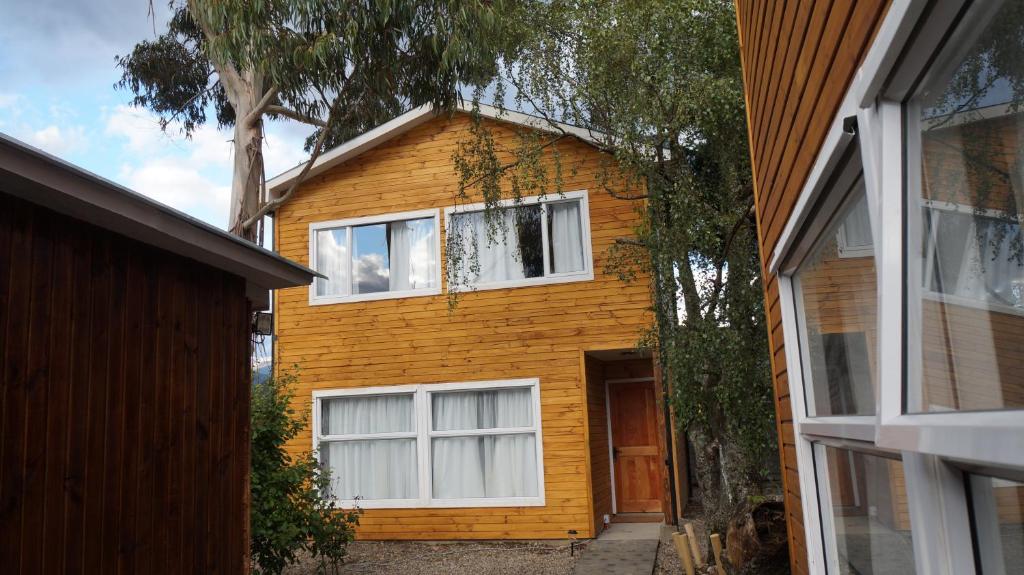 una casa amarilla con ventanas blancas y un árbol en Patagonia Oley, en Puerto Aysén