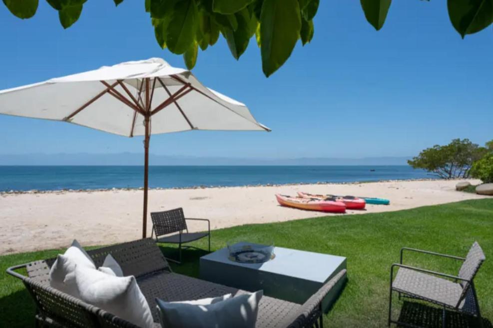 a patio with an umbrella and chairs and a beach at Porta Fortuna Villa Punta Mita Gates in Punta Mita