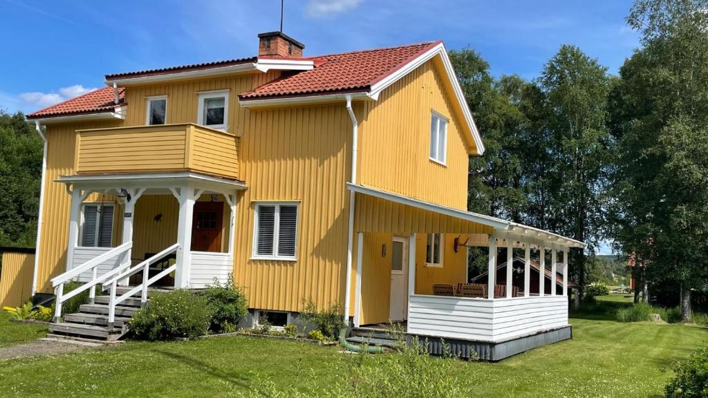 a yellow house with a porch and a yard at Beloni 122 in Gustavsfors