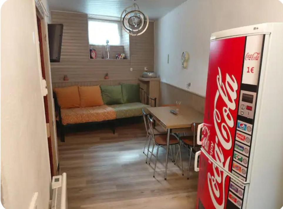a living room with a cocacola refrigerator and a table at Le nid douillet Vintage idéal pour 2 jusqu'à 4 in La Bourboule