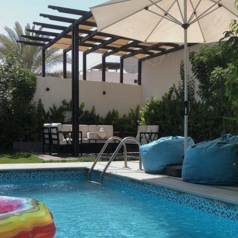 a swimming pool with an umbrella next to a swimming pool at شاليهات دبليو العمارية W Chalet in Al ‘Ammārīyah