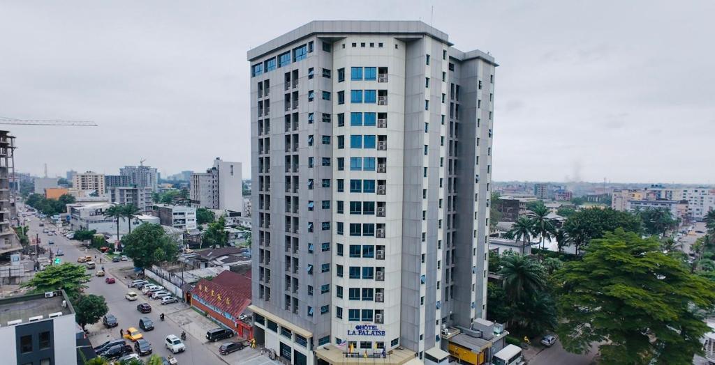 a tall white building with blue windows in a city at Hotel La Falaise Bonapriso in Douala