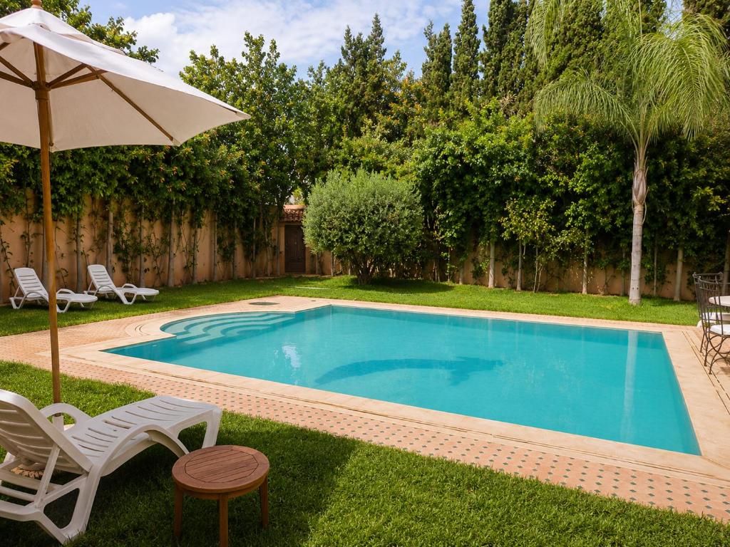 a swimming pool with an umbrella and chairs and a table at Villa des Perles in Marrakesh