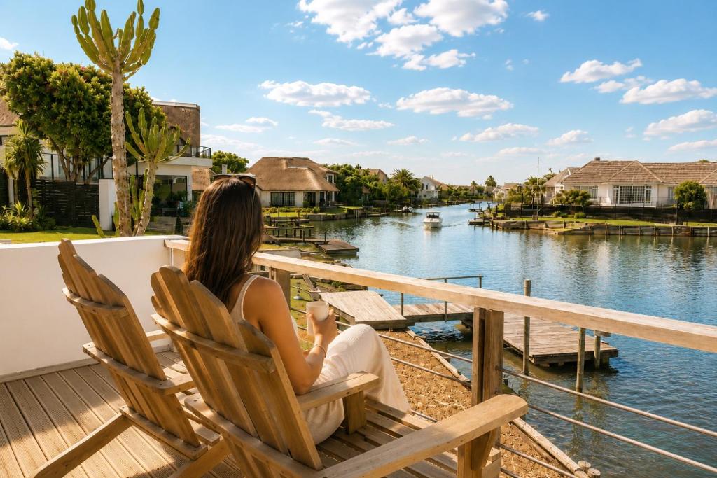 a woman sitting in a chair on a deck overlooking a river at CANAL GUEST HOUSE - Waterfront Boutique B&B in St Francis Bay
