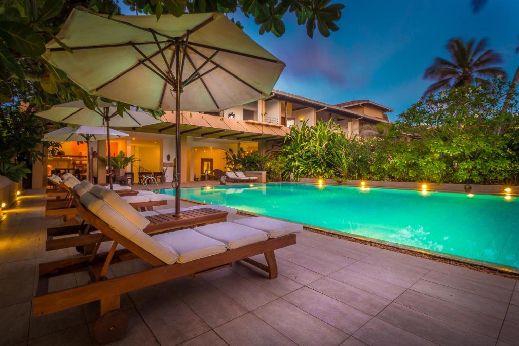 a pool with chairs and an umbrella next to a house at Aditya Resort in Hikkaduwa