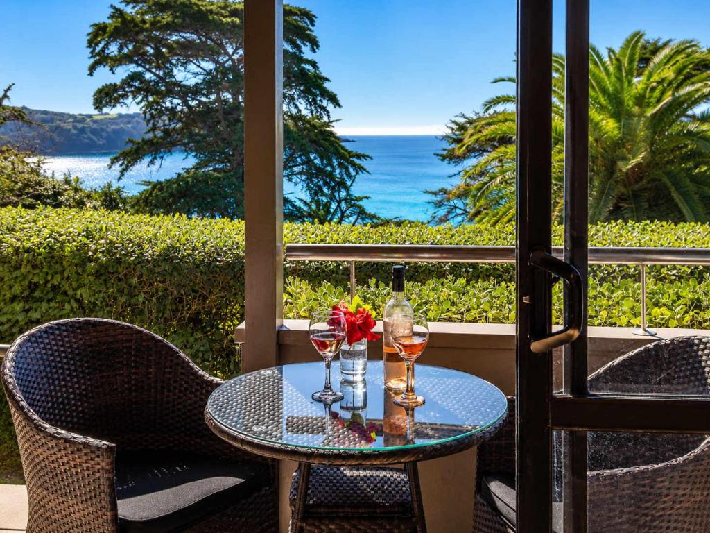 a table with wine glasses and flowers on a patio at Aqua Sands #1 - Stay Waiheke in Oneroa