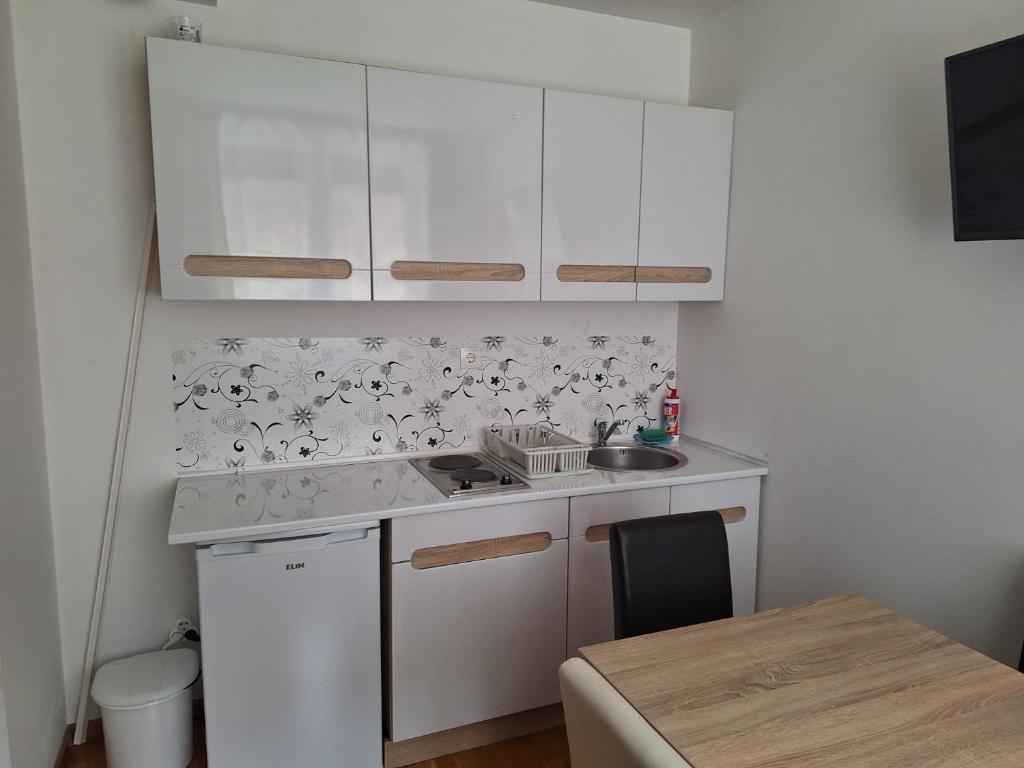 a kitchen with white cabinets and a sink and a table at Apartman Glorija in Brzeće