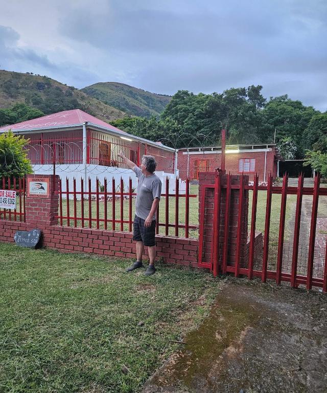 a man standing next to a red fence at Blessed home by the Mountain surrounded macadamia in Barberton