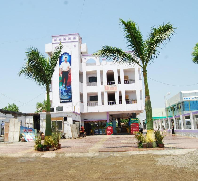 a white building with palm trees in front of it at Hotel Utsav in Shirdi