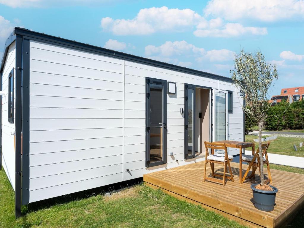 a small white tiny house with a wooden deck at Caravan Bredene on the coast in Bredene