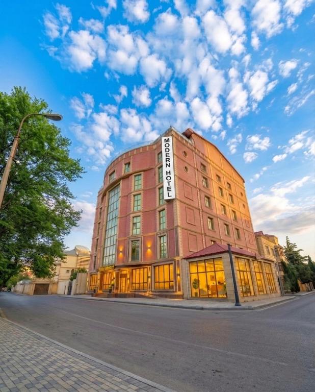 ein rotes Gebäude in einer Straße mit bewölktem Himmel in der Unterkunft Modern Hotel Baku in Baku