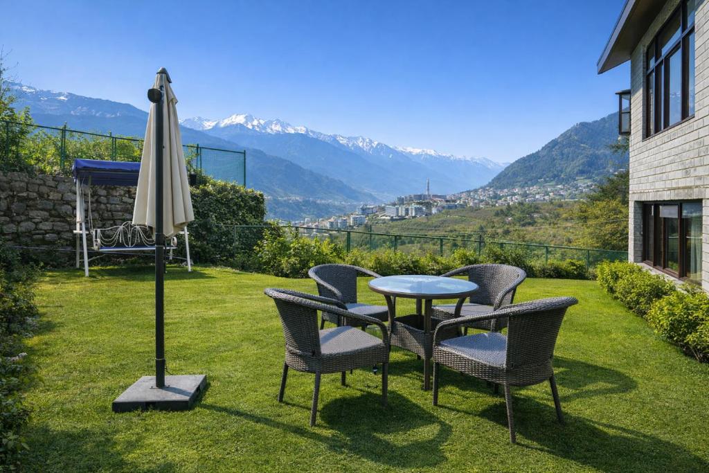 a table and chairs and an umbrella on a lawn at The Himalayan Nomad Manali - 2 bedrooms mountain view independent villas with personal lawn in Manāli
