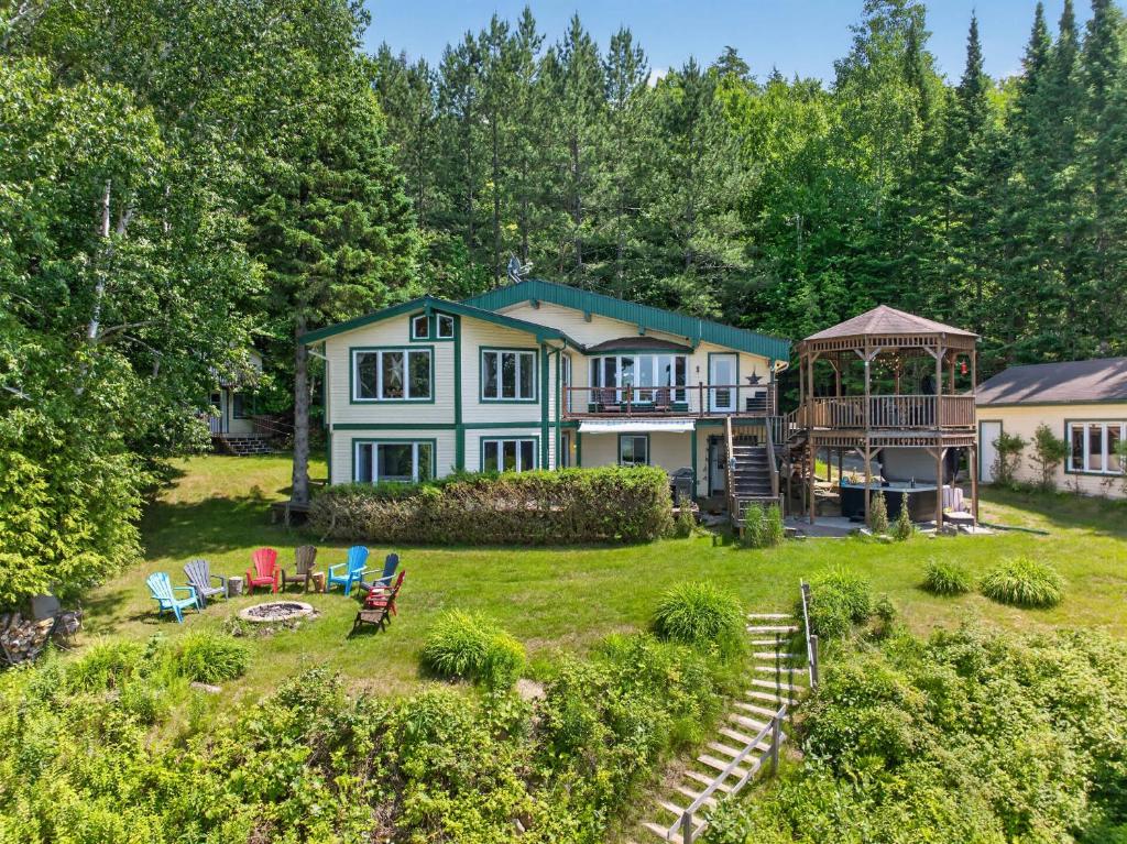 a large house with a yard with chairs and a gazebo at Spa & Waterfront - Chalet le Colibri in Saint-Rémi-dʼAmherst