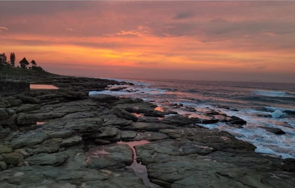 a sunset on a rocky beach with the ocean at Laguna La Crete 33 in Uvongo Beach