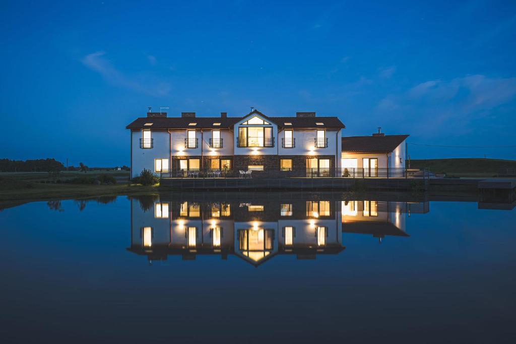 a house with lights on the water at night at Sodyba Pelėdų medus in Vainekoniai