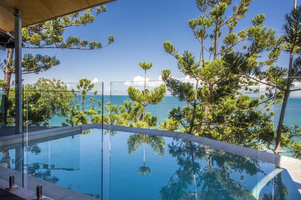 a swimming pool with trees and the ocean in the background at Headland House in Picnic Bay