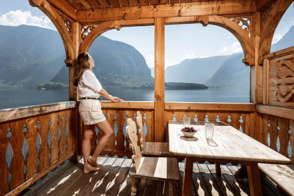 a woman standing on a wooden balcony looking out at a lake at Seehaus 96 Hallstatt in Hallstatt