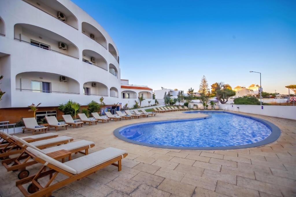a resort with a swimming pool and chairs and a building at Hotel Maritur - Adults Only by Pierre & Vacances in Albufeira