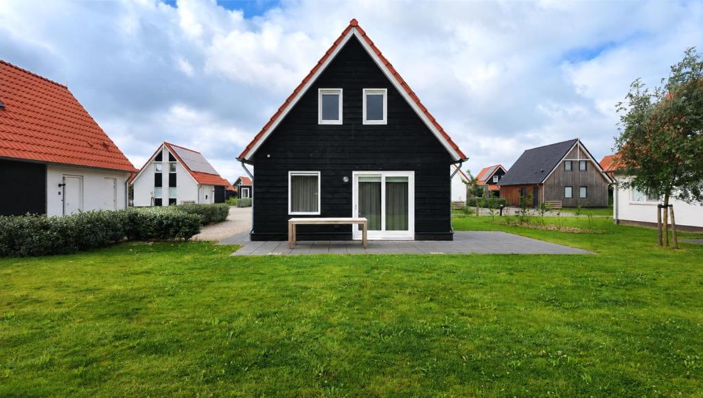 a black house with a bench in a yard at Villapark Wulpdal | Villa De Wulp in Scherpenisse