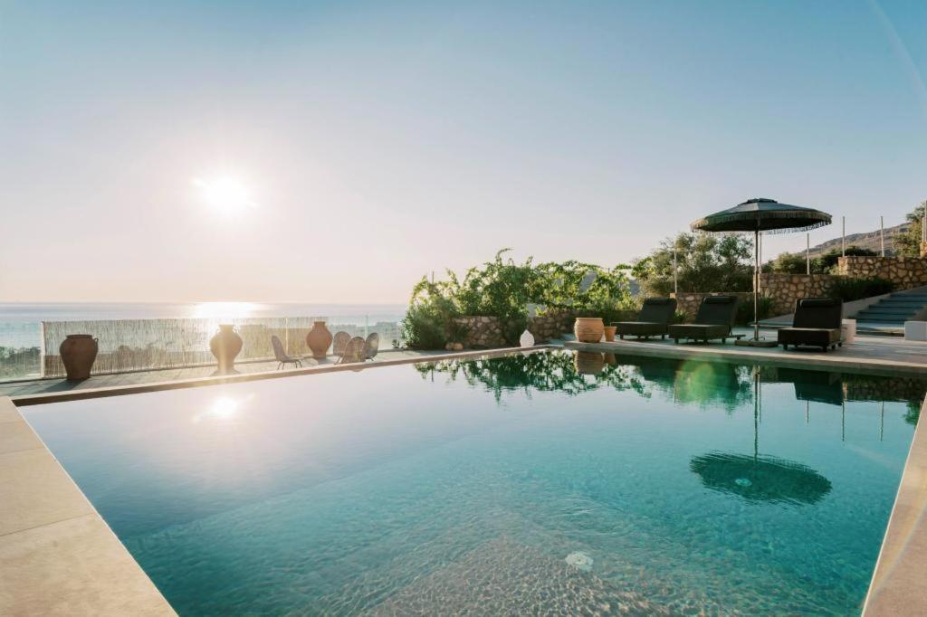 a swimming pool with an umbrella and chairs and the ocean at Michelle Villa in vlicha