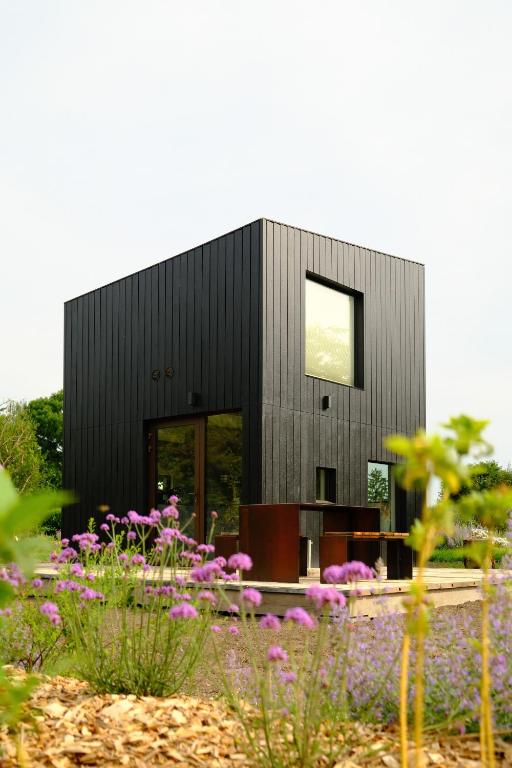 a black house with purple flowers in front of it at Oseraie Cabins - Wild lodges entre Liège et Maastricht in Visé